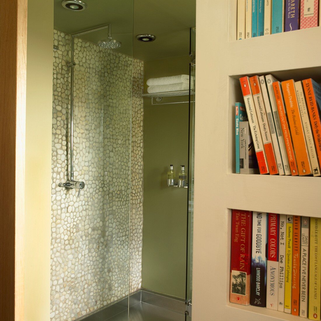 Green shower stall with mosaic tile wall and glass door next to a bookcase