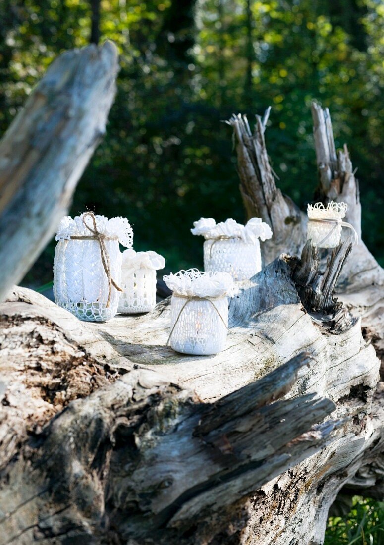 Candle lanterns made from glass jars with lace covers on weathered tree stump in sunshine