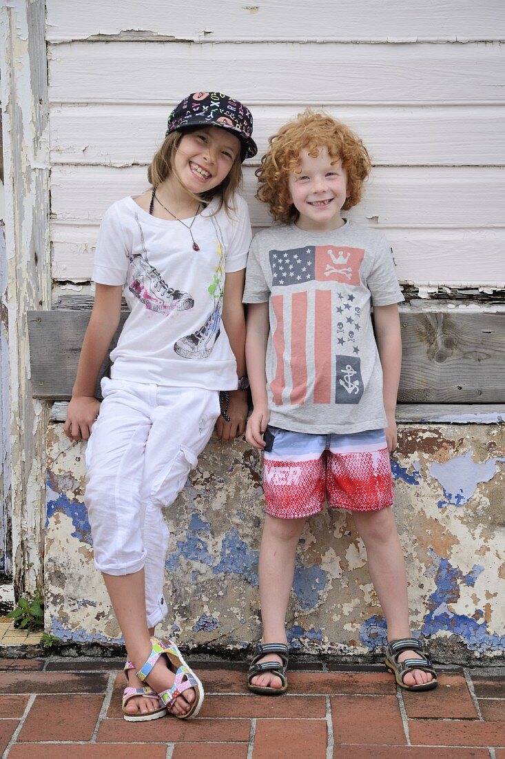 Zwei Kinder lehnen an verwittertem Steinsockel eines alten Holzhauses