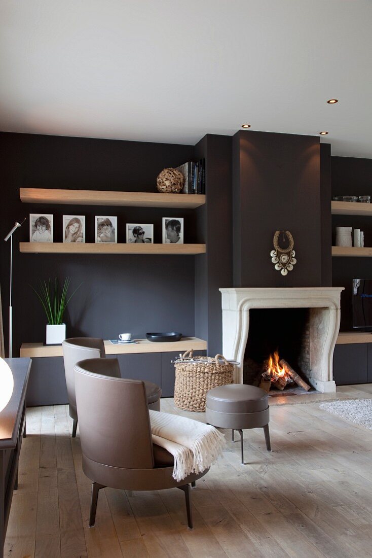 Klassisch moderne Sesseln mit grauem Lederbezug vor offenem Kamin und schwarz getönter Wand in elegantem Wohnzimmer