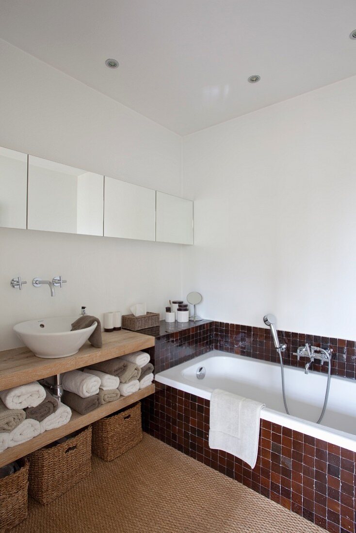 Waschschüssel auf Holzplatte unter modernem Spiegelschrank und Badewanne