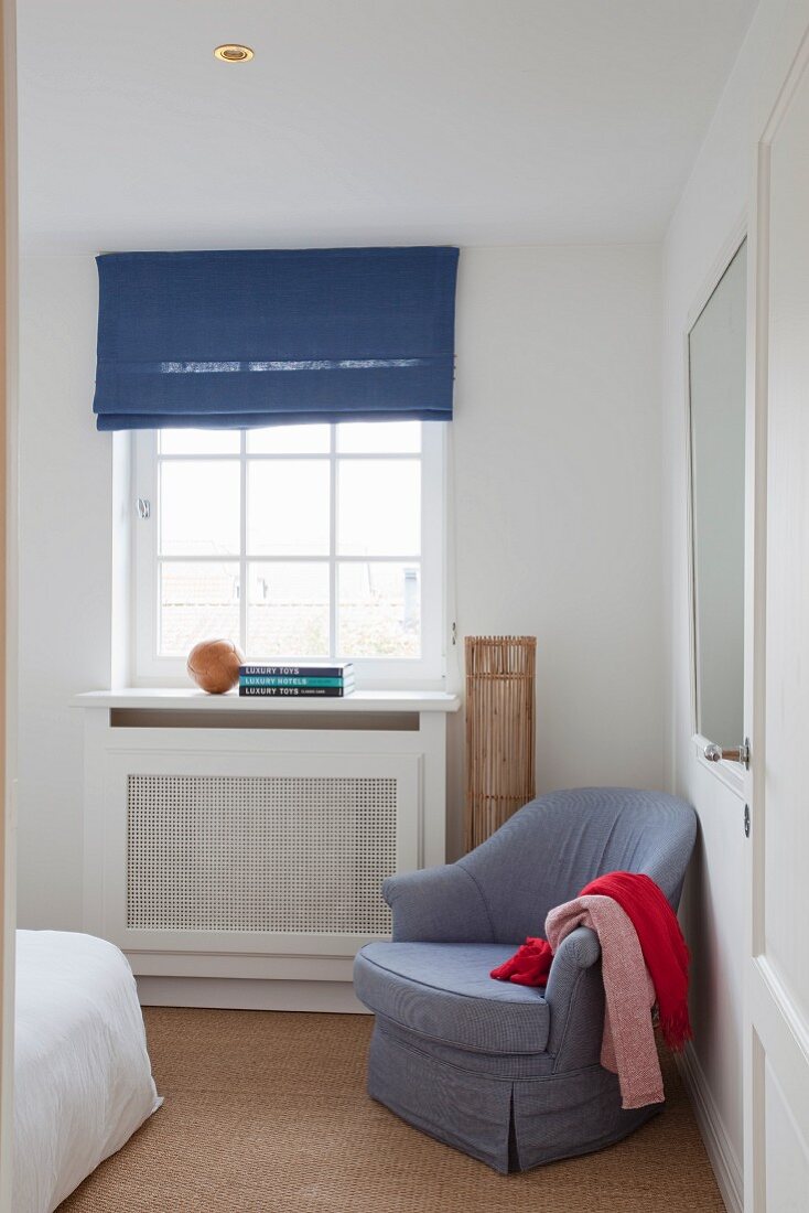 Pale blue armchair next to lattice window with dark blue Roman blind in corner of bedroom