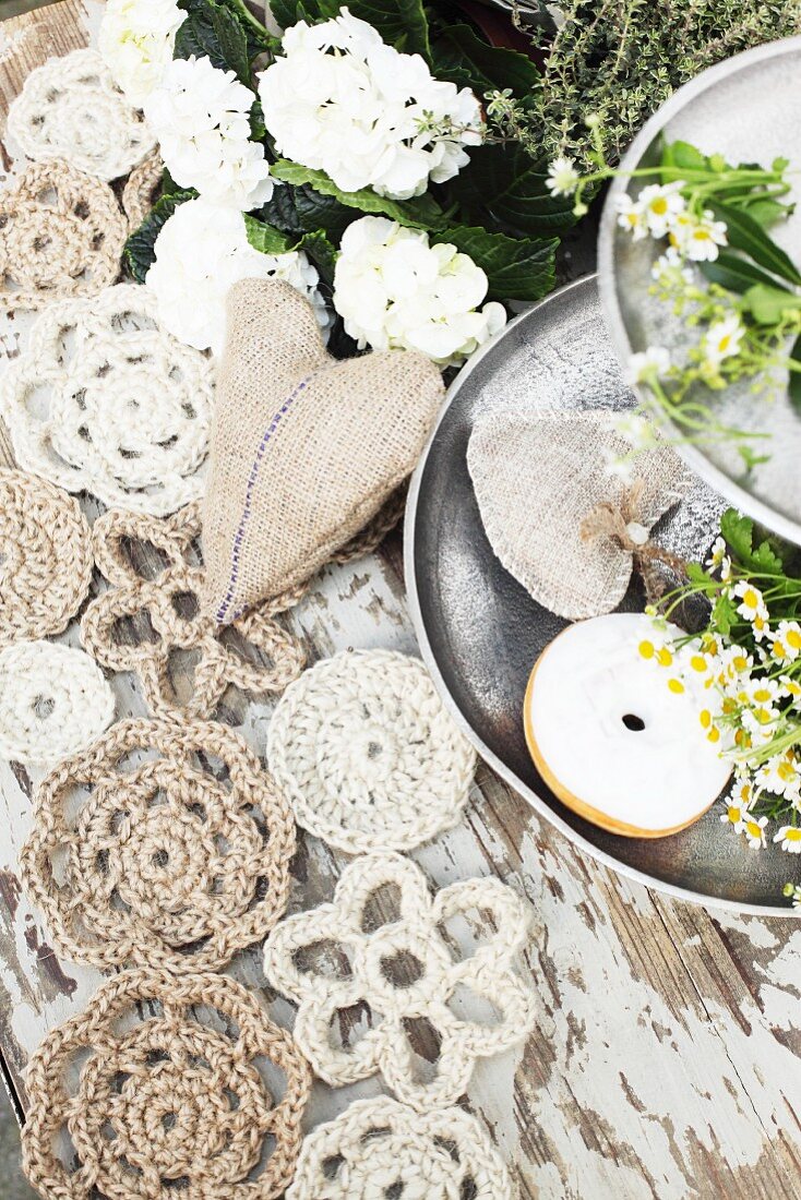 Doilies hand-crocheted from jute yarn and hessian heart next to doughnut and chamomile on metal cake stand
