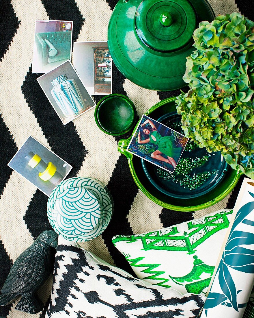 Arrangement verschiedener Keramikdosen, Dekorationsartikel in Grüntönen und Fotos auf schwarz-weißem Teppich