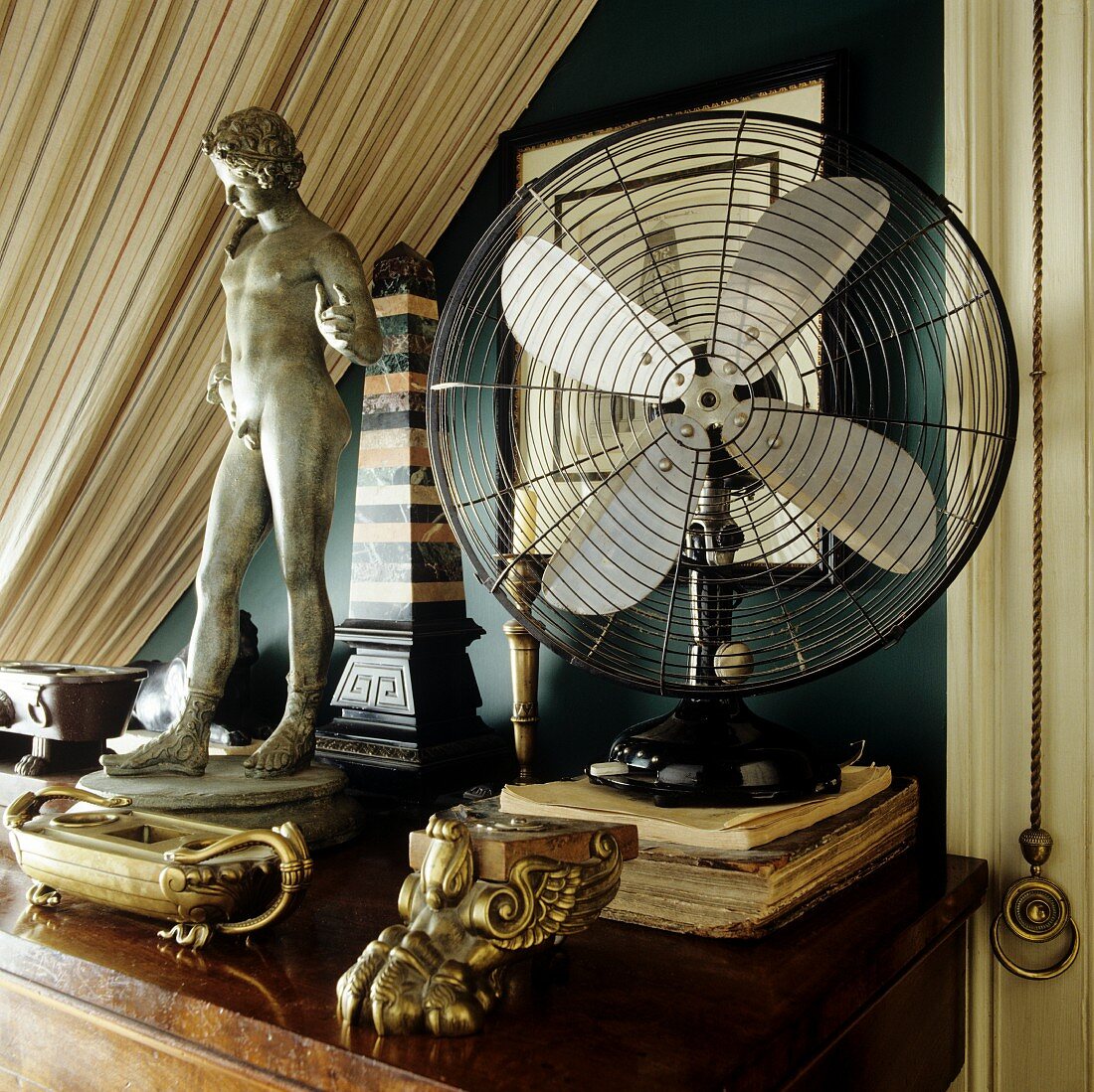 Brass ornaments and antique, miniature stone figurine next to fan on wooden table