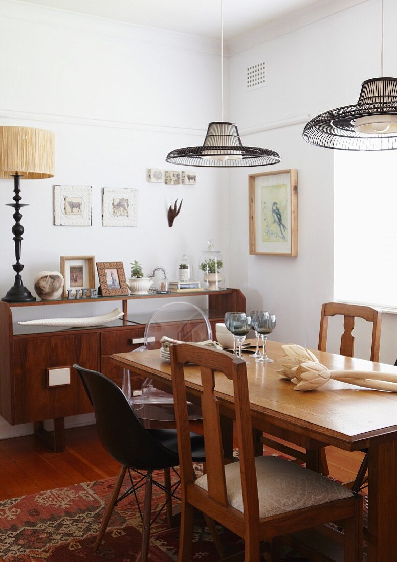 Wooden dining table and various chairs below pendant lamps with slatted lampshades