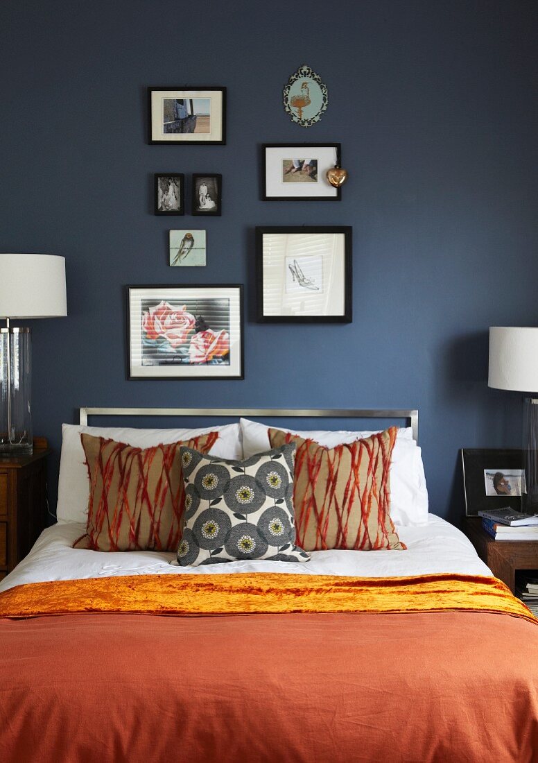 Double bed with rust red bedspread and scatter cushions against dark-painted wall