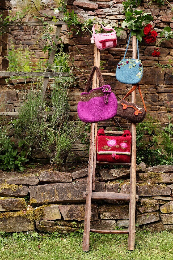Verschiedene selbstgemachte Filztaschen auf Leiter an Steinmauer