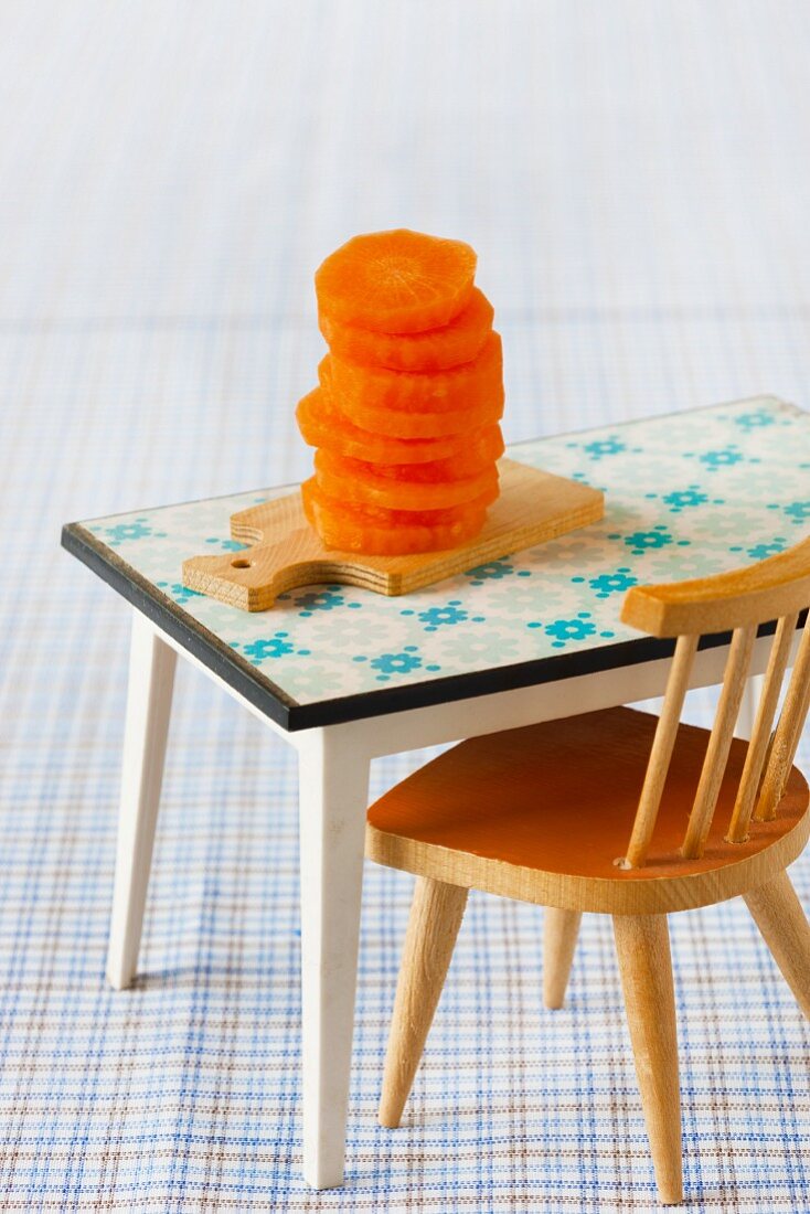 Small stack of sliced raw carrots on miniature chopping board with dolls' house furniture
