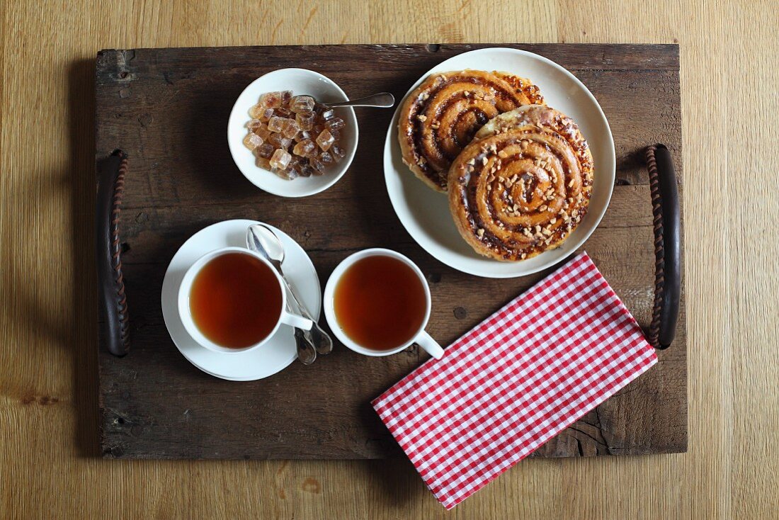 Teller mit Nussschnecken, Teetassen und Kandiszucker auf Holztablett mit selbstgemachten Ledergriffen