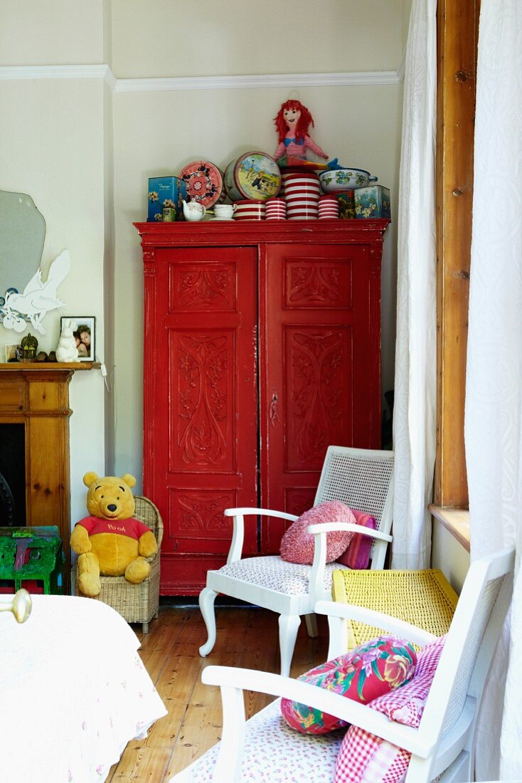 weiße Stühle mit bunten Kissen vor rot lackiertem Schrank in Kinderzimmerecke