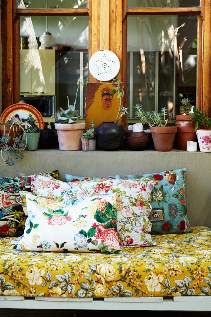 Floral cushions and mattress on couch in front of potted plants on window sill
