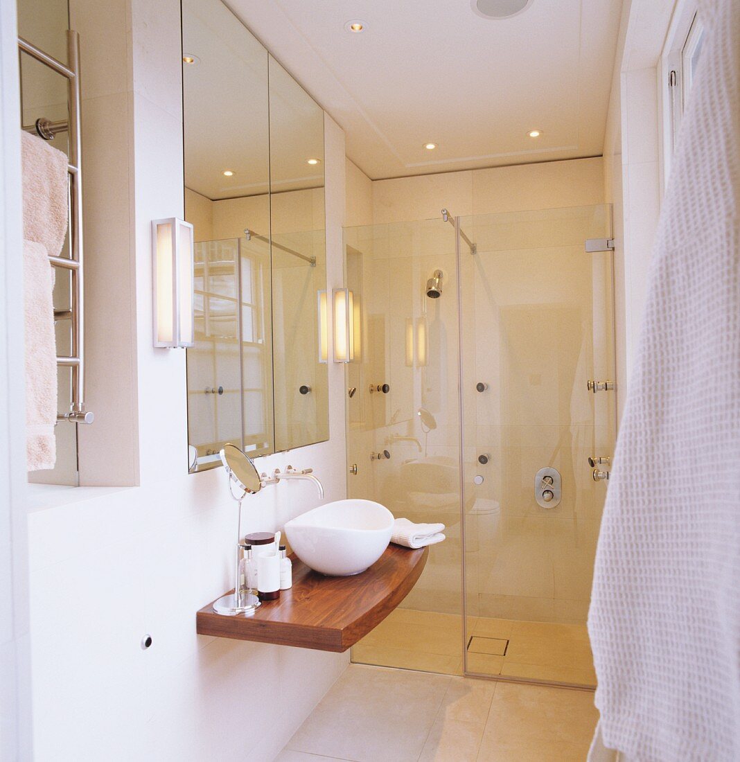Designerbad mit kleinem Waschtisch auf Holzplatte vor verglastem Duschbereich