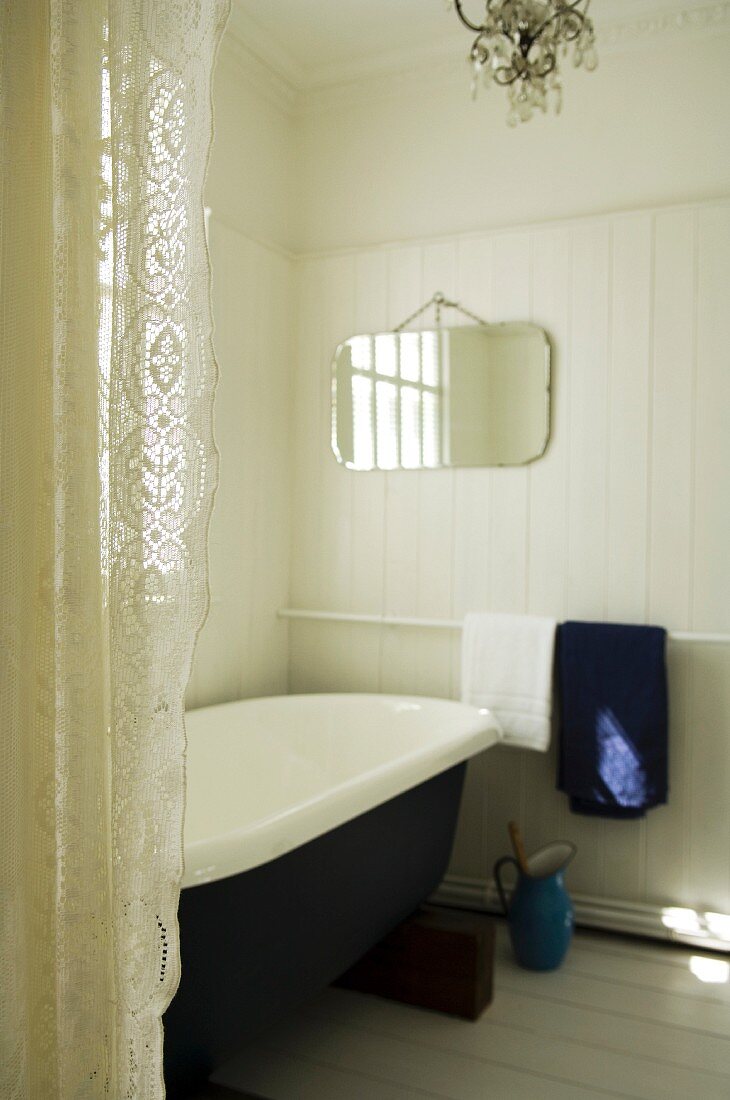 Vintage Badewanne mit weißer Holzverkleidung an Wand, seitlich Spitzenvorhang