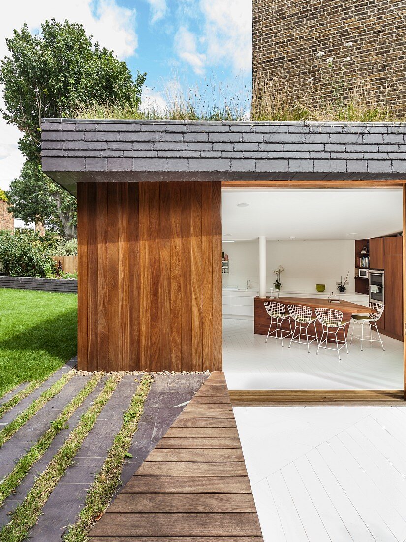 Blick von der Terrasse in modernen Wohnraum mit Küchentheke aus Edelholz und Barstühlen im Bauhausstil