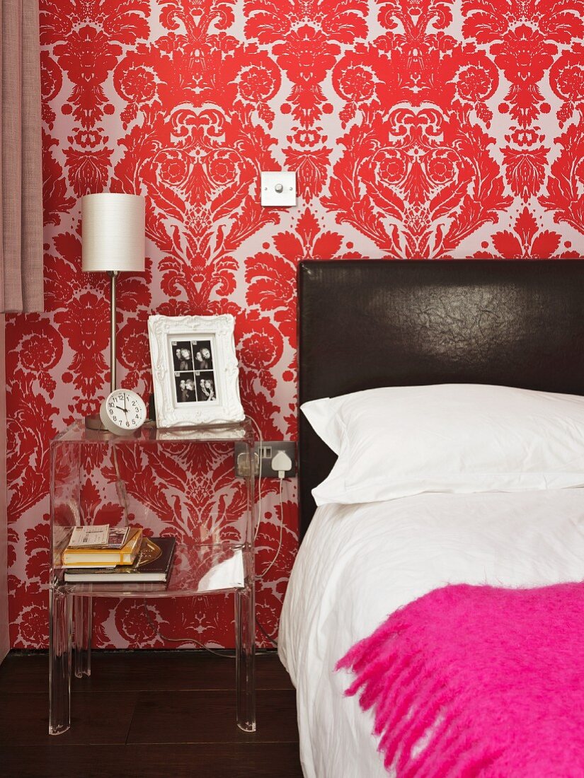 Bed with black leather headboard and pink blanket across foot against red and white wallpaper