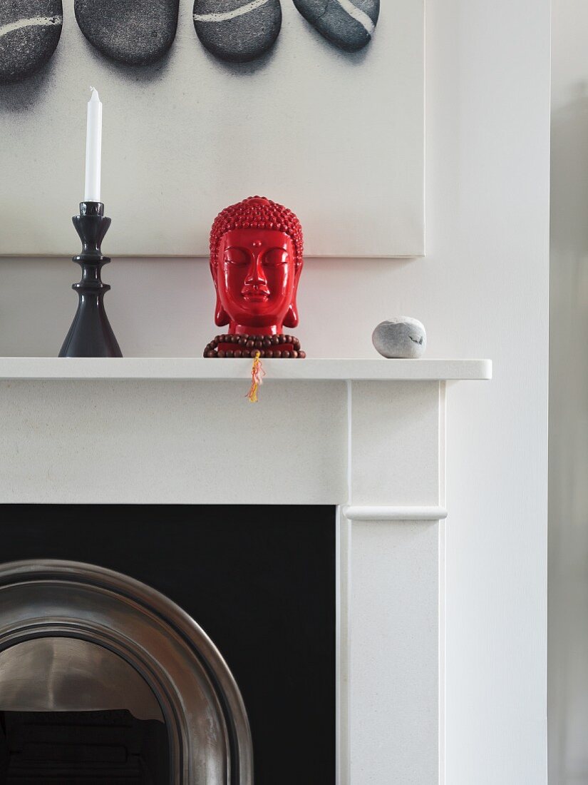 Red, ceramic head of Buddha next to black candlestick on mantelpiece