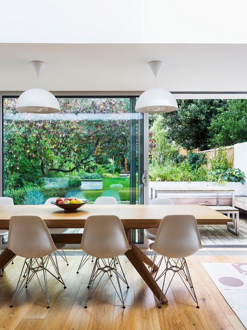 Stuhlklassiker und moderner Esstisch aus Holz vor offener Terrassentür mit Blick auf Gartenterrasse und Garten
