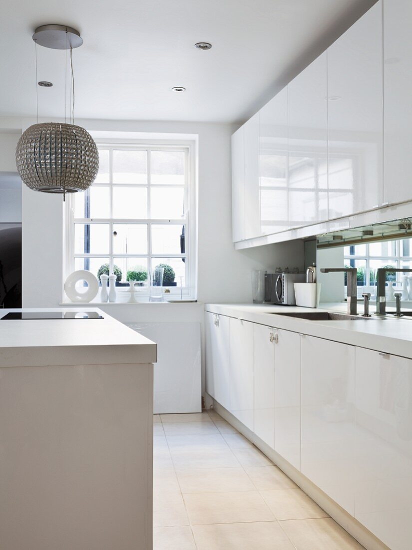 White kitchen counter with mirrored splashback and spherical lamp above island unit
