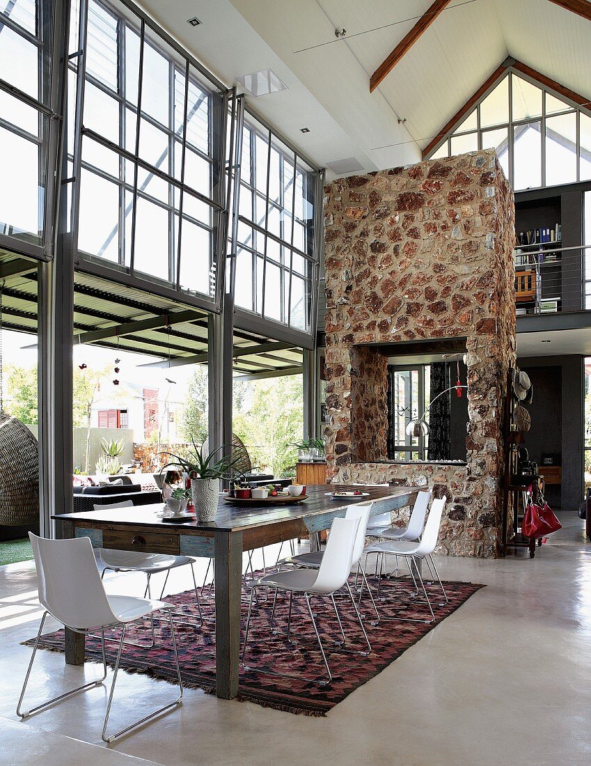Wohnraum im Industriestil mit verglasten Fensterfronten & eingebautem Kamin in Trennwand aus Natursteinen