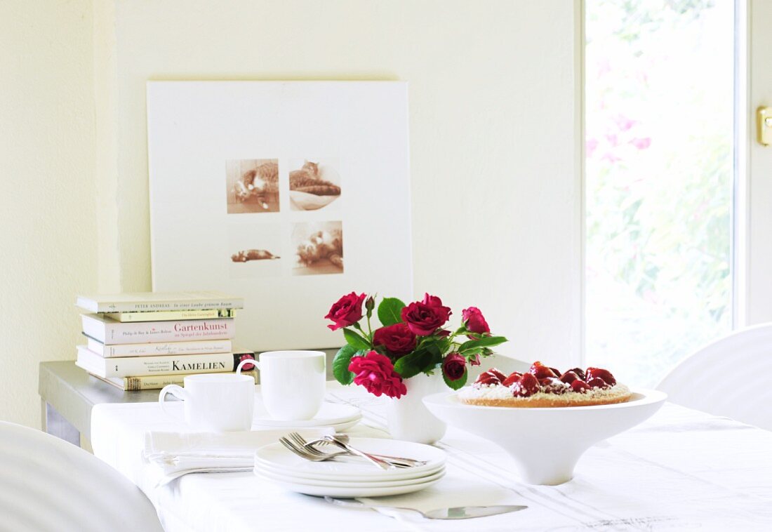 Gedeckter Tisch mit Erdbeerkuchen, Rosenstrauss, Kaffeegeschirr und Büchern