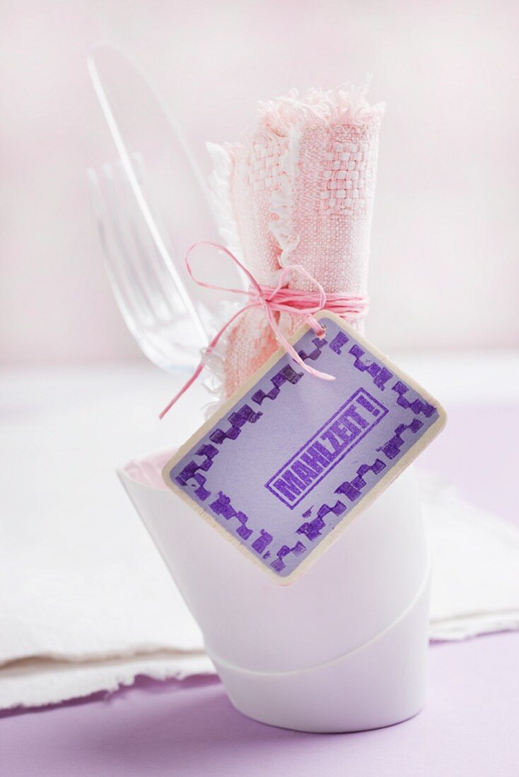 Plastic cutlery and pink linen napkin in beaker; wooden tag with rubber-stamped lettering and border
