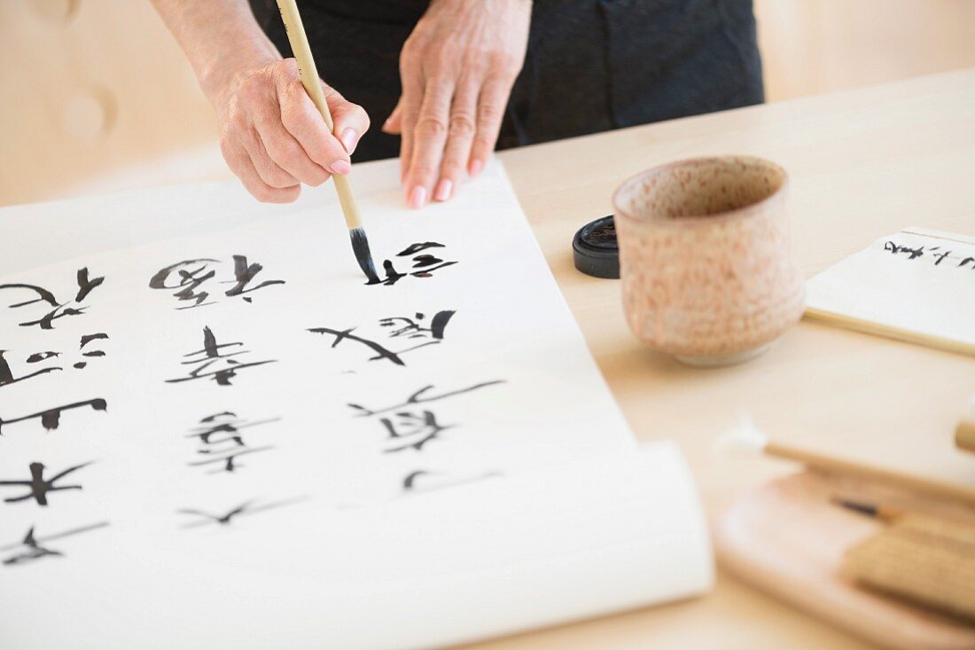 Frau malt mit Pinsel asiatische Schriftzeichen auf Papierrolle