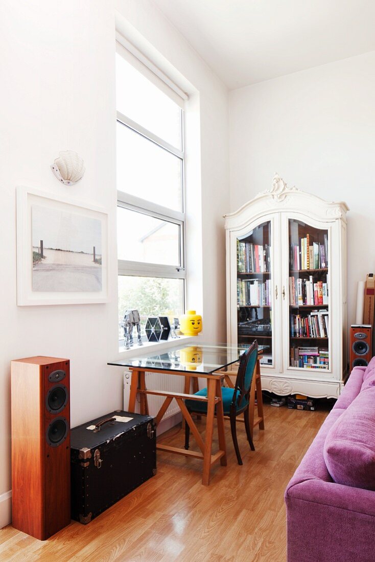 Stilmix in Wohnraum mit Glastisch vor großen Loftfenstern, Vitrinenschrank im Rokokostil & violettem Samtsofa