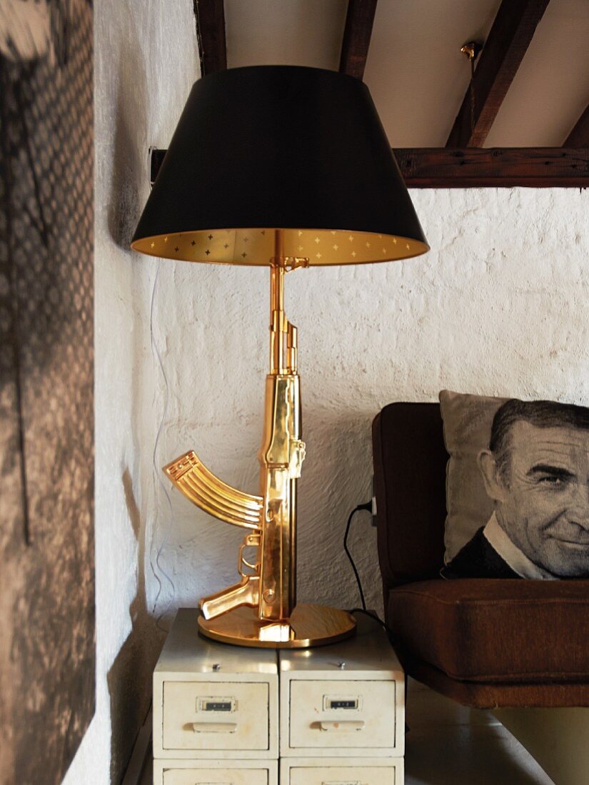 Table lamp with antler-shaped brass base on small drawer units next to armchair with photo-print cushion