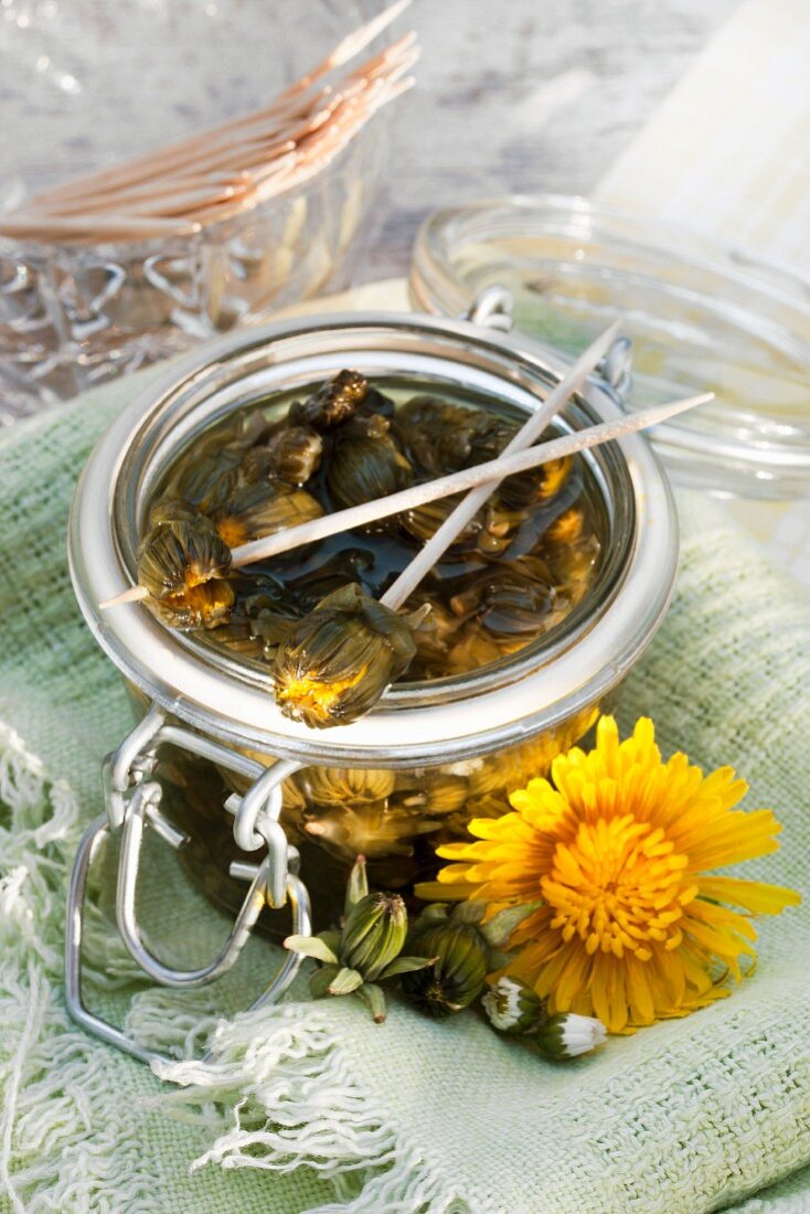 Glass jar of mock capers made from pickled dandelion and daisy buds; two skewered on cocktail sticks