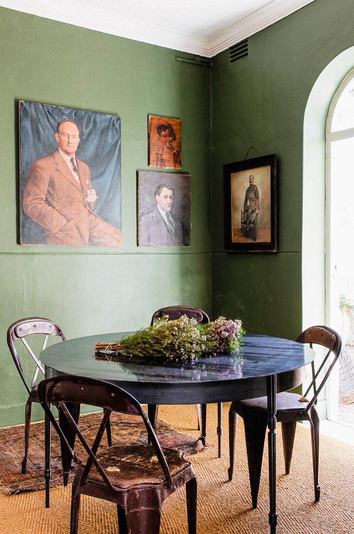 Retro metal chairs at round table in corner of green-painted room with paintings on wall