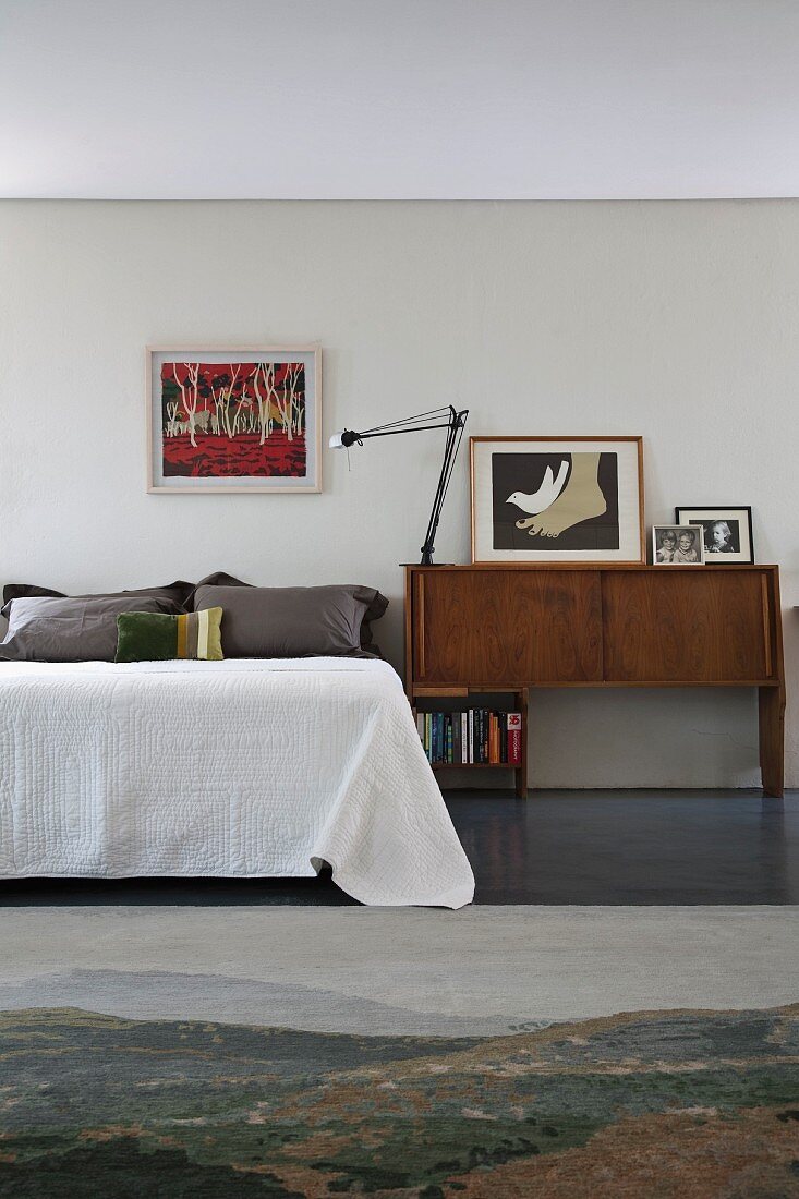 60s sideboard, contemporary art and photographs next to bed with bedspread
