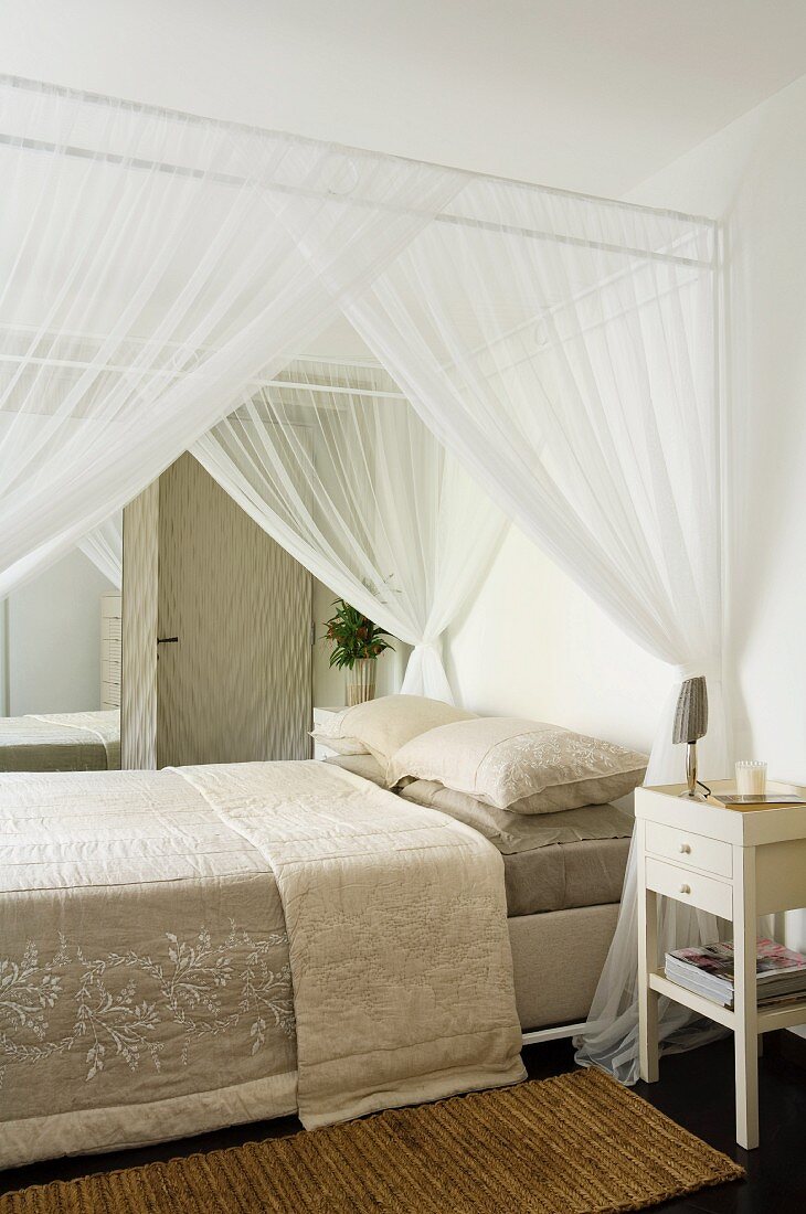 Elegant, four-poster bed with pale bedspread and airy canopy