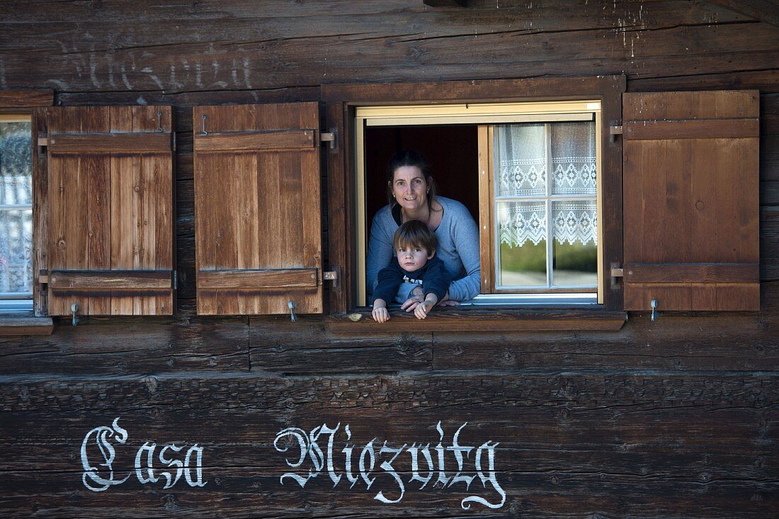 Frau mit Kind am Fenster eines Holzhauses