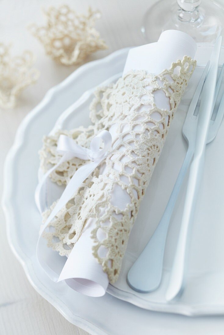 Menu rolled up in crocheted doily and cutlery on set of plates