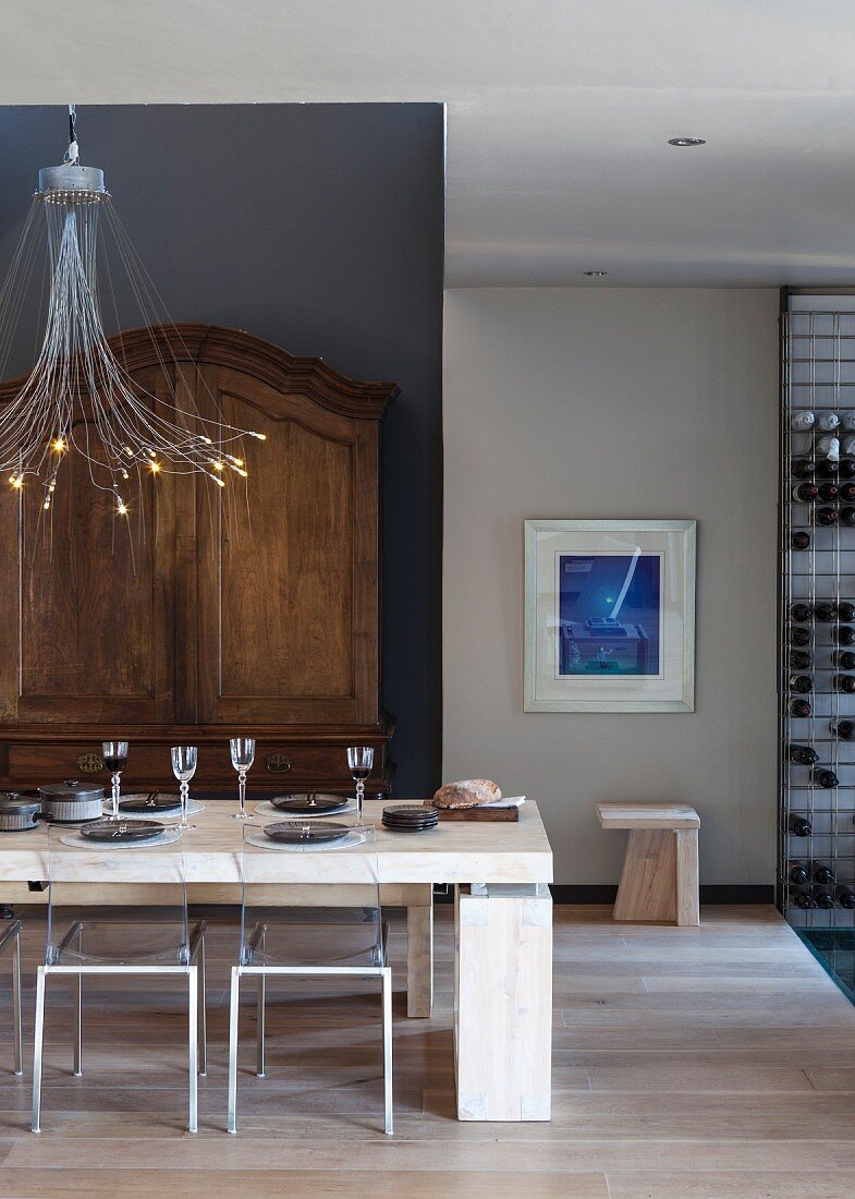 Moderner gedeckter Esstisch unter Designer Hängeleuchte vor antikem Schrank an schwarzer Wand