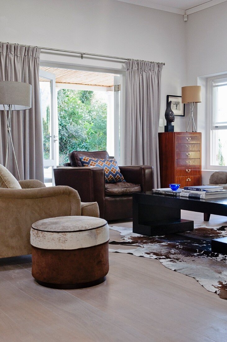 Round pouffe and various armchairs around coffee table on cowhide rug in living room