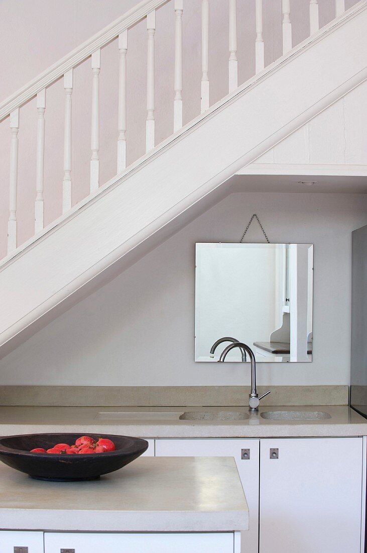 Küchenblock vor Küchenzeile in Nische unter Treppenlauf mit weiss lackiertem Holzgeländer