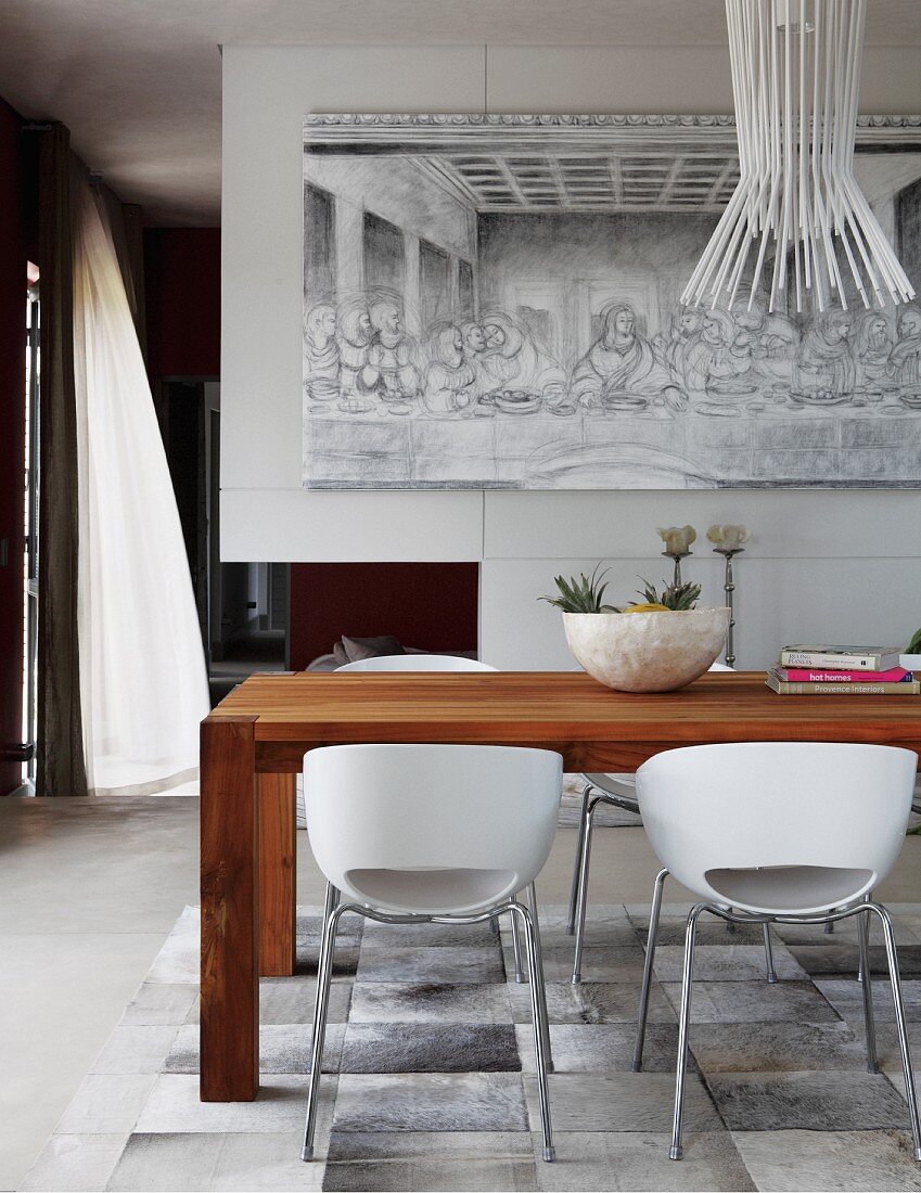 White shell chairs around wooden table below designer pendant lamp; Last Supper painting in black and white on wall