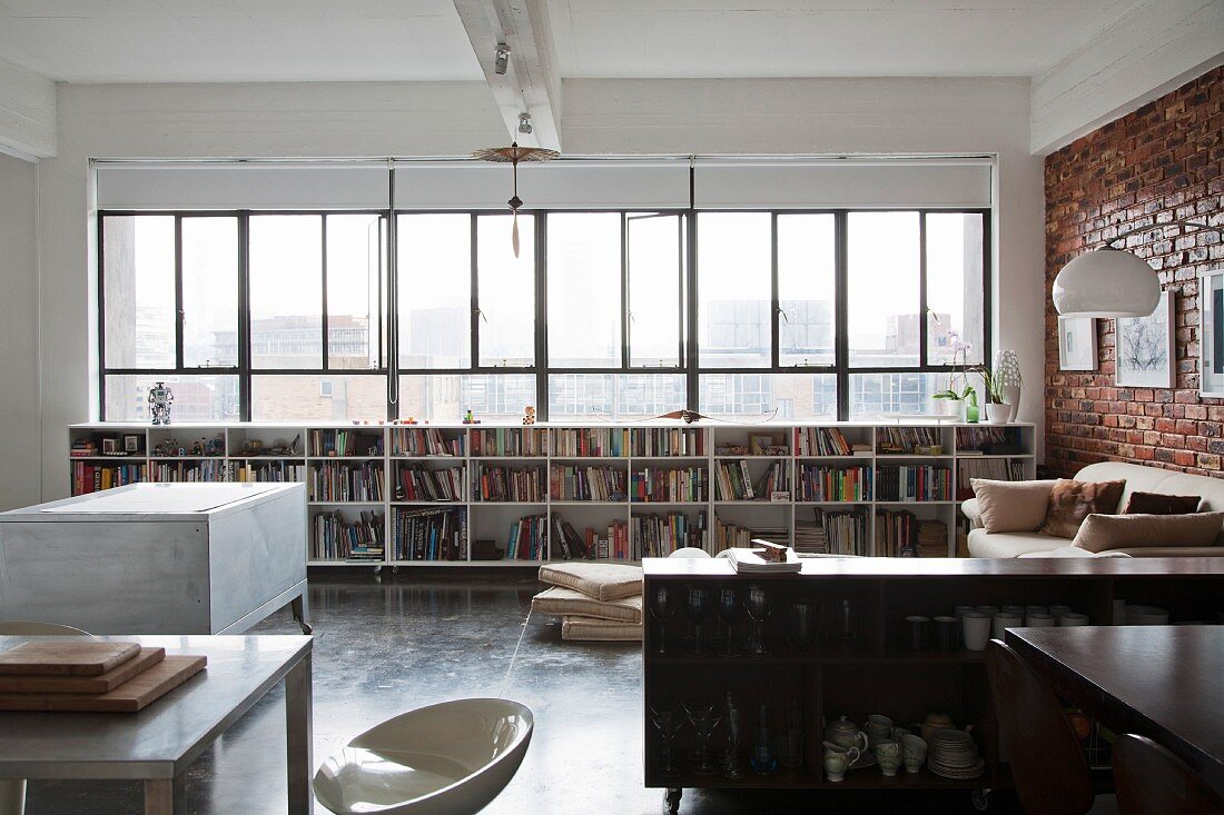 Offener Küchenbereich mit Sideboard, gegenüber Regal mit Büchern unter Fensterband in loftartigem Wohnraum