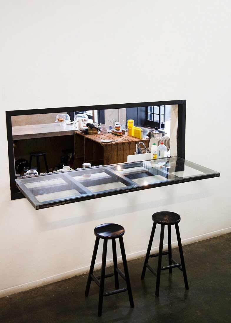 Black barstools at glass panel counter top in serving hatch with view into kitchen