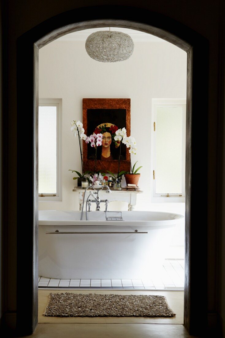 Blick durch Durchgang auf freistehende Badewanne und Ablage mit Blumen & Wandbild