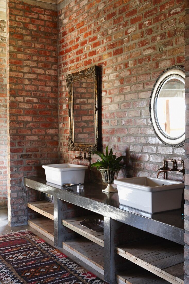 Waschschüsseln auf Regalunterbau vor Ziegelwand, darüber Vintage-Spiegel mit Metallrahmen