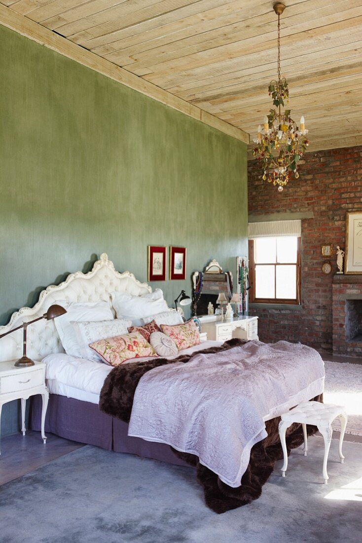 Double bed with upholstered, Baroque-style headboard against green wall in rustic bedroom with brick wall and wooden ceiling