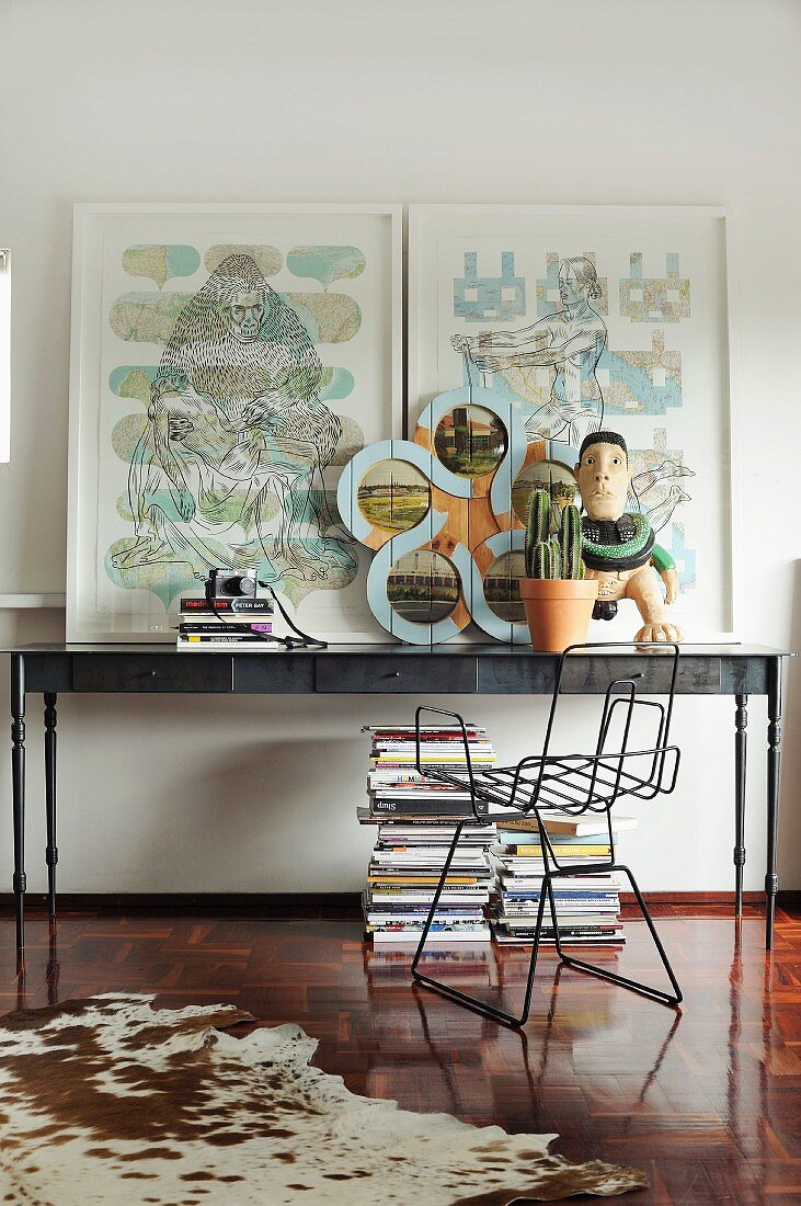 Kuhfell auf Parkettboden und Metallstuhl vor postmodernem Wandtisch mit Bildern und Kunstobjekten