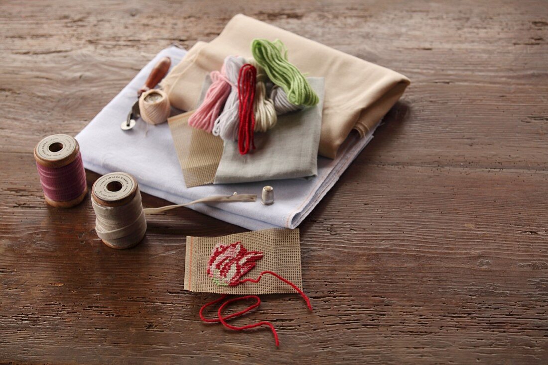 Reels of yarn, hand-embroidered sample and various fabrics on rustic wooden surface