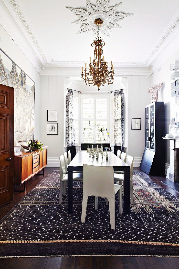Schwarzer Tisch und weiße Stühle unter Kerzenleuchter und Stuckelementen an Decke in eklektizistischem Esszimmer