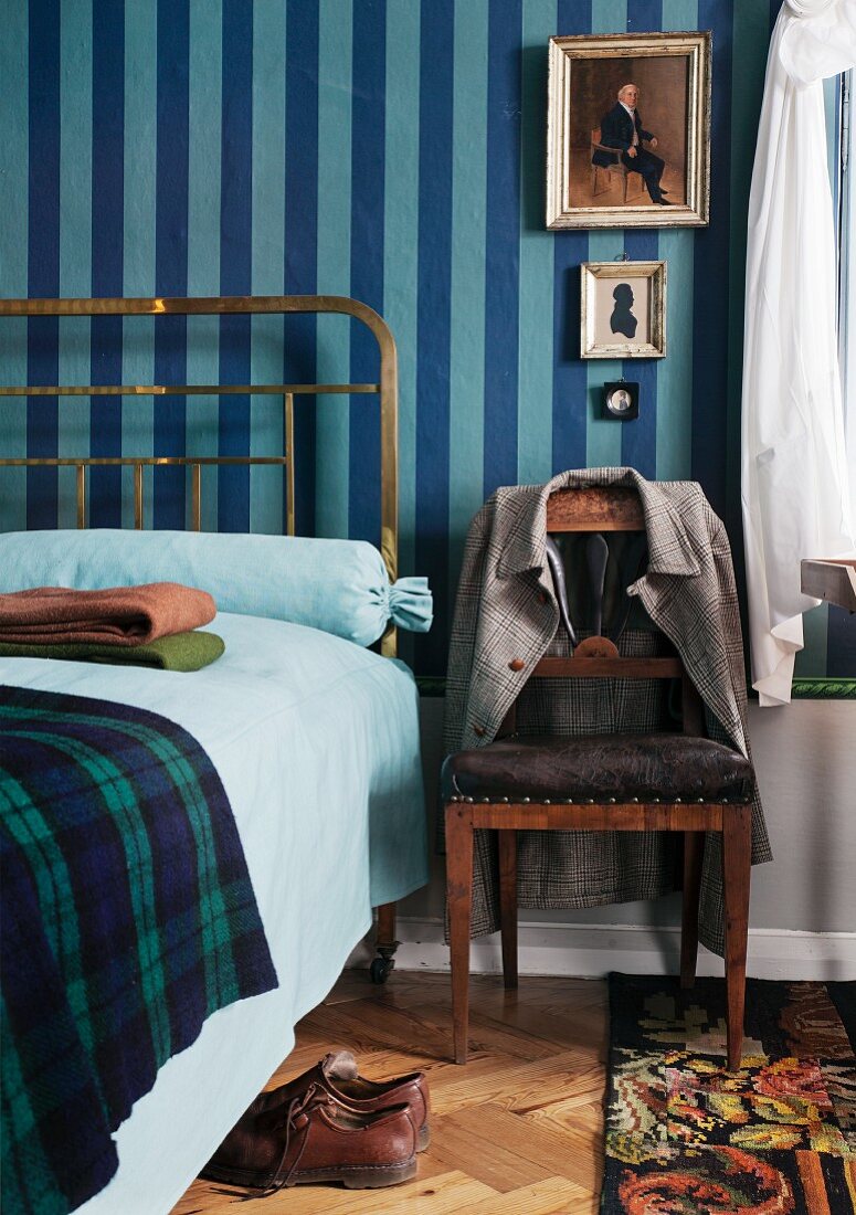 Period brass bedstead and Biedermeier chair against blue striped wallpaper