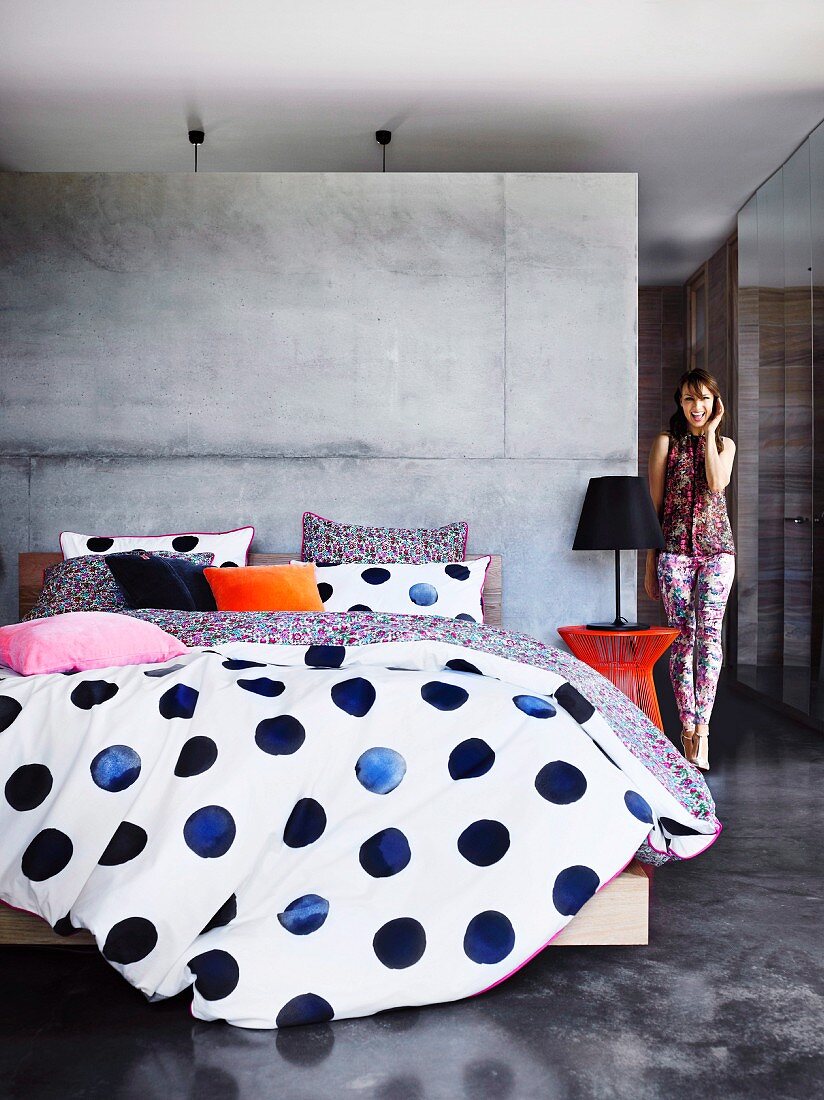 Bettwäsche mit blauen Punkten auf Doppelbett vor Betonwand als Raumteiler in minimalistischem Schlafbereich