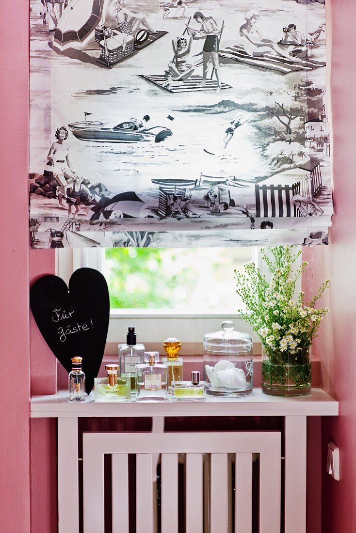 Roman blind with black and white print at bathroom window and bottles of perfumes for guests